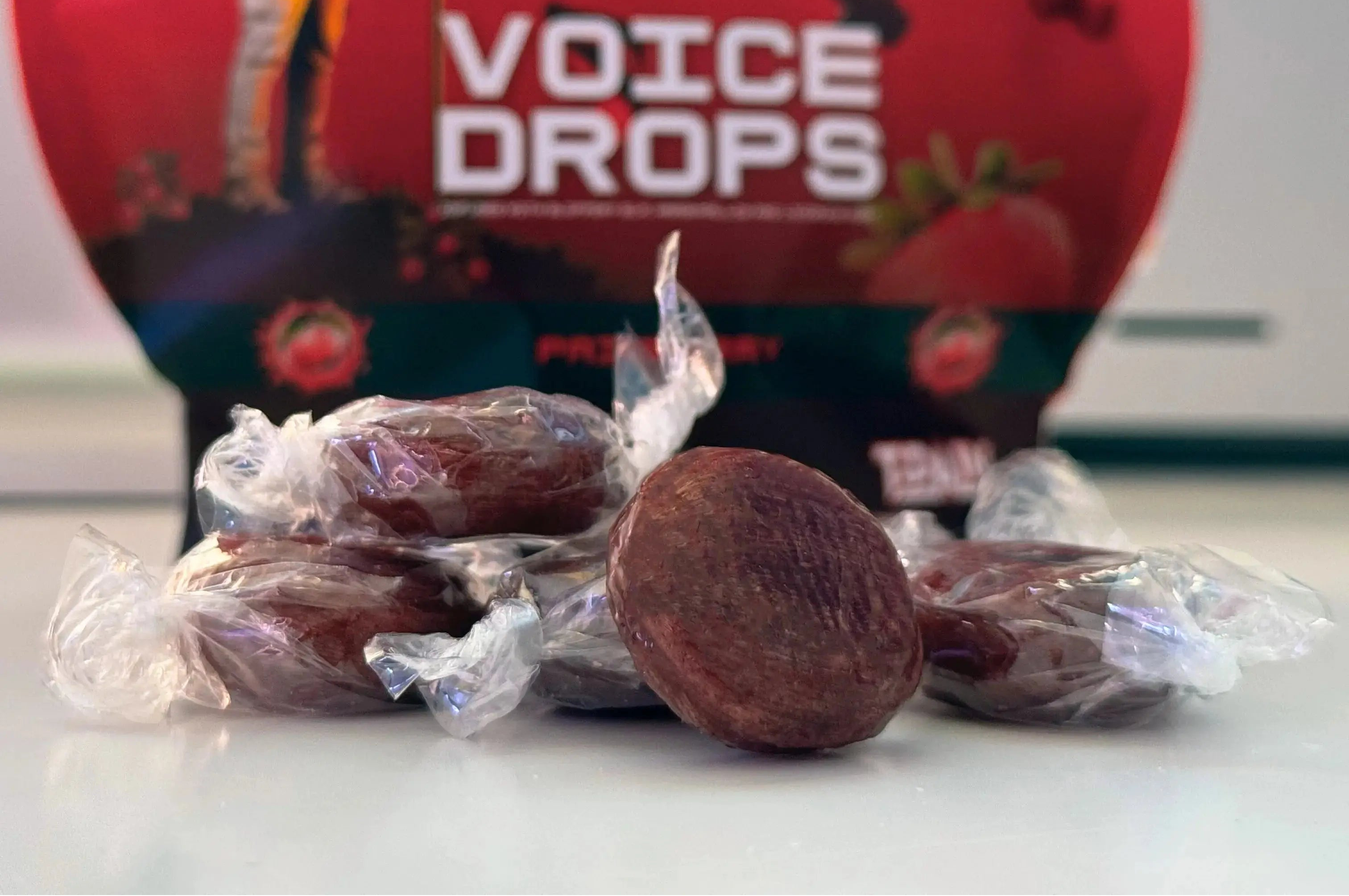 Red 'One Shot Voice Drops' package with wrapped red berries on a white surface